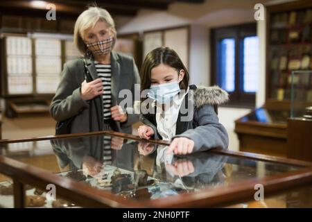 Tween écolière et femme âgée tutrice en masques de visage observant l'exposition dans la galerie d'art Banque D'Images