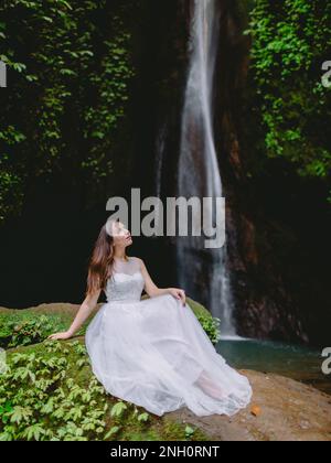01 juin 2022. Bali, Indonésie. Femme en robe de mariage assise sur la pierre près de la cascade dans les montagnes. Banque D'Images