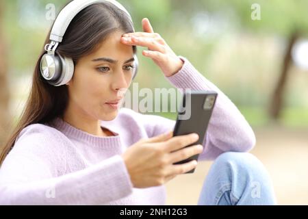 Une femme a surpris de regarder les médias au téléphone dans un parc Banque D'Images