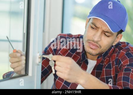 un menuisier installe la serrure de porte à l'aide d'un tournevis sans fil Banque D'Images