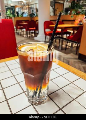 Délicieux café froid. Cocktail frais avec glace, tranches de citron et pailles. Le cappuccino froid est sur une table à carreaux blancs. Intérieur du café à l'arrière Banque D'Images