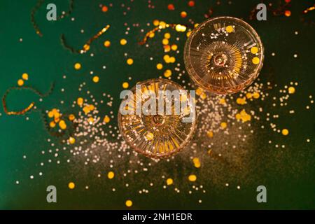 Deux verres de champagne exquis avec des paillettes argentées et des confettis. Élégant cocktail alcool sur fond vert avec serpentin d'or et paillettes. Banque D'Images