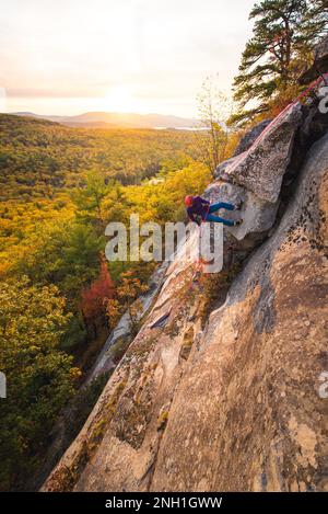 Grimpeur de roche, qui fait une descente en rappel avec des montagnes et des feuillages en arrière-plan Banque D'Images