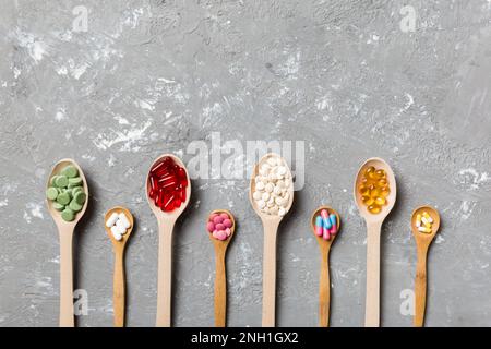 Vue de dessus variété de pilules de vitamines et de minéraux dans une cuillère en bois sur fond coloré. Vue de dessus d'un assortiment de pilules pharmaceutiques. Régime alimentaire Banque D'Images