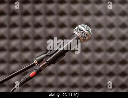 Microphone contemporain placé dans la salle de répétition contre un mur noir texturé flou avec mise au point sélective Banque D'Images