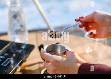 Une main de femme avec une cuillère de café moulu est remplie d'une cafetière geyser rétro sur une table en bois. Café Moka. Banque D'Images