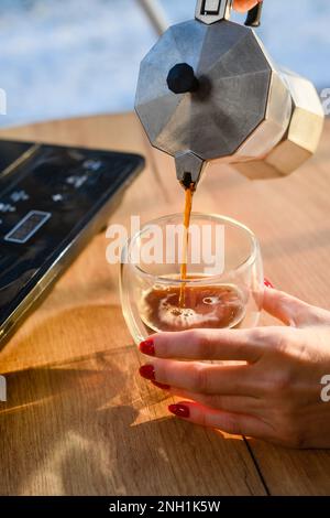 Une jeune fille verse du café fraîchement préparé dans une tasse transparente. Café Moka. Banque D'Images
