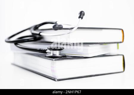 Stéthoscope à l'écoute de livres de médecine empilés. Arrière-plan blanc avec espace de copie. Concept isolé d'apprentissage et d'étude de la médecine, de la cardiologie, de la santé Banque D'Images