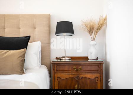 Chambre élégante avec table de chevet baroque, ornements complexes et monogrammes. Sur la table de chevet est lampe de nuit avec abat-jour noir et vase avec Banque D'Images