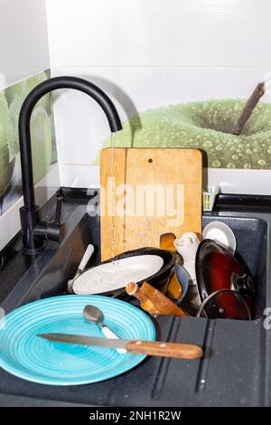 Un évier de cuisine avec un robinet ouvert avec de l'eau courante et une montagne de plats sales. Lavage de la vaisselle. Banque D'Images