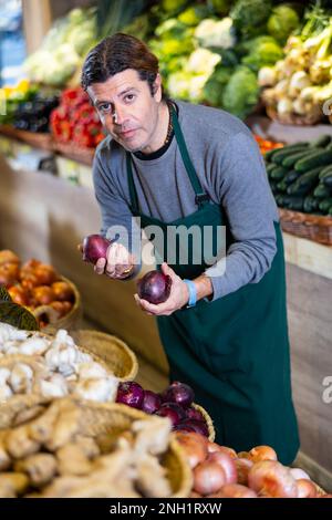 Un travailleur d'épicerie de sexe masculin organise l'oignon rouge et les autres légumes sur le comptoir Banque D'Images