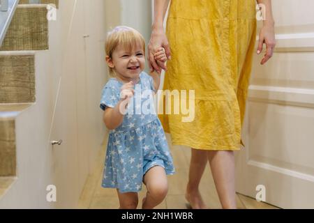 La petite fille émotive s'amuse à la maison en tenant la main de sa mère. Banque D'Images