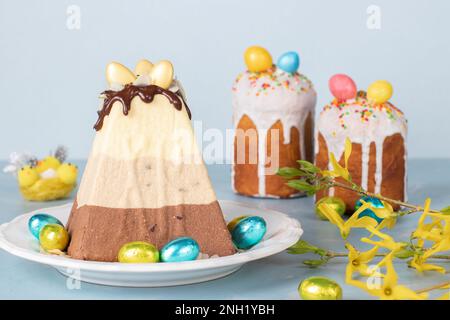 Dessert traditionnel caillé de Pâques fait de trois types de chocolat - blanc, lait et foncé et ainsi que deux gâteaux de Pâques sur fond bleu Banque D'Images