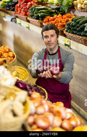 Un travailleur d'épicerie de sexe masculin organise l'oignon rouge et les autres légumes sur le comptoir Banque D'Images