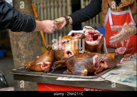 Carcasses de chiens rôties placées sur la table devant l'acheteur anonyme qui paie au vendeur de cultures sur le marché vietnamien local Banque D'Images