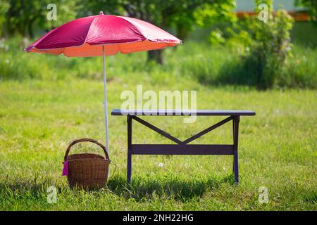 Pour un pique-nique. Sur un pré vert il y a une table en bois, un panier en osier et des zones du soleil. Banque D'Images