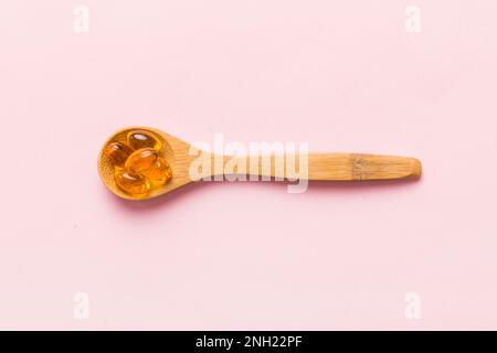 Capsules de vitamine omega dans une cuillère sur un fond coloré. Pilules servi comme un repas sain. Capsules rouges de supplément de vitamine en gel doux sur la cuillère. Banque D'Images