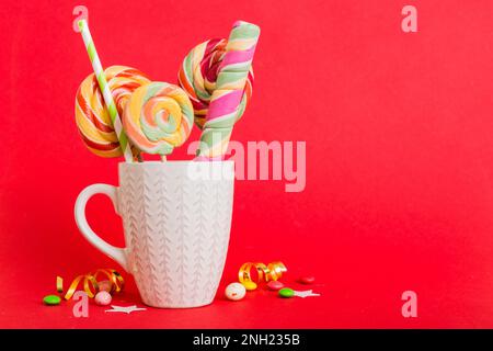 Bonbons colorés dans une tasse sur une table sur fond clair. Grands sucettes tournantes. Concept créatif d'un pot rempli de délicieux bonbons de la Banque D'Images