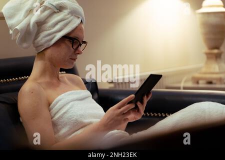 Jeune fille avec des lunettes de vue lisant détendu après la douche, la routine de beauté, à la maison Banque D'Images