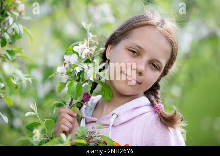 27 mai 2021. Biélorussie, Gomel, événement public.Une belle adolescente avec des queues de porc pose sur le fond d'un pommier en fleur. Banque D'Images