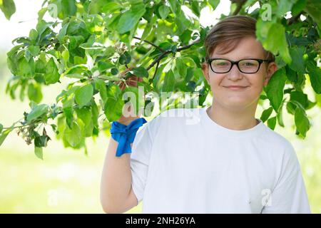 27 mai 2021. Biélorussie, Gomel, événement public.beau garçon de l'adolescence avec des lunettes dans le jardin de printemps. Portrait en gros plan d'un enfant avec branches d'arbre vertes. Banque D'Images