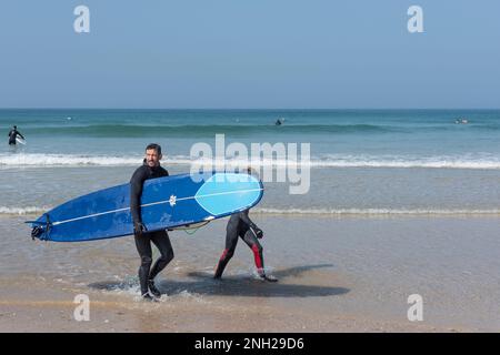 Un père et son fils portant leur planche de surf après avoir surfé à Fistral Beach par une chaude journée ensoleillée à Newquay, en Cornouailles. Banque D'Images