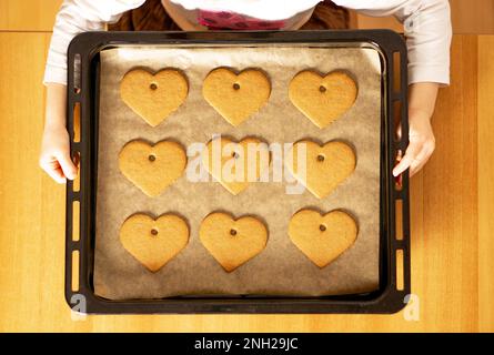 Beaucoup de petits gâteaux de coeur frais faits maison sur une plaque de cuisson dans les mains d'une fille. Concept de la Saint-Valentin. Photo de haute qualité. Banque D'Images