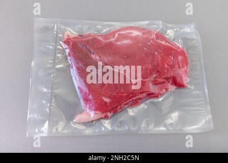 Steak de bœuf cru dans un emballage scellé sous vide pour la cuisson sous vide sur fond gris Banque D'Images