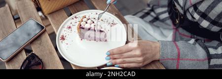 Vue de dessus sur la femme avec manucure bleue manger cheesecake avec cappuccino à la table à l'extérieur. Banque D'Images