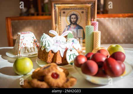 Gâteau de Pâques avec œufs peints, pommes et biscuits sur la table dans la cuisine. Icônes de l'église et bougie en arrière-plan. Thème de la religion orthodoxe. Banque D'Images