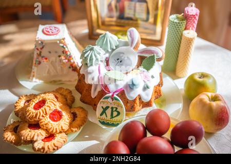 Gâteau de Pâques avec œufs peints, pommes et biscuits sur la table dans la cuisine. Icônes de l'église et bougie en arrière-plan. Thème de la religion orthodoxe. Banque D'Images