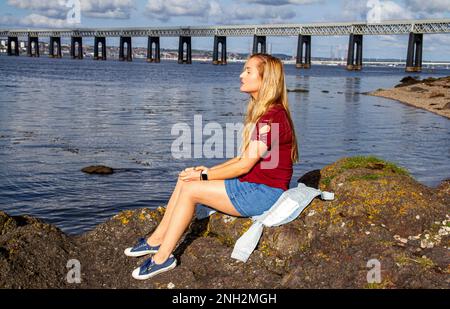 Lors d'une belle journée d'octobre à Wormit Beach, Fife, Rhianna Martin se trouve sur de grandes rochers au bord de la rivière Tay, en Écosse Banque D'Images