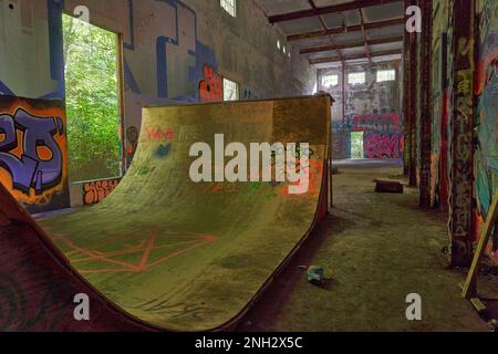 Grande rampe de planches à roulettes en contreplaqué dans un ancien bâtiment abandonné avec les murs sont recouverts de graffiti Banque D'Images