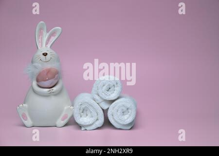 Sculpture d'un lapin blanc avec des œufs de Pâques sur fond rose avec des serviettes blanches. Banque D'Images