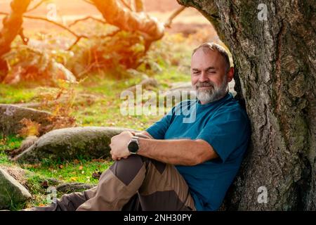 Barbu homme en bottes spéciales atteignant la destination et se reposant sous l'arbre dans Peak District au coucher du soleil le jour de l'automne Travel Lifestyle concept Banque D'Images