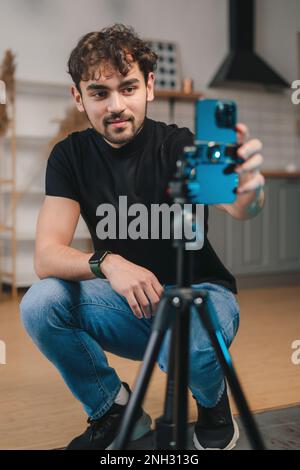 Un blogueur d'homme caucasien excité qui diffuse depuis sa maison, partage son style de vie avec ses adeptes, en utilisant un smartphone sur trépied. Enregistrement d'homme d'affaires en ligne Banque D'Images