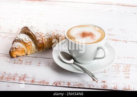 Petit déjeuner avec cappuccino et croissant sur table en bois. Banque D'Images