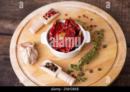 Tomates séchées à l'huile d'olive dans un bol blanc avec poivre, ail et thym sur une planche de bois. Cuisine maison, style rustique. Mise au point sélective, gros plan Banque D'Images