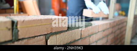 Un constructeur professionnel pose des briques et construit un mur dans l'appartement Banque D'Images