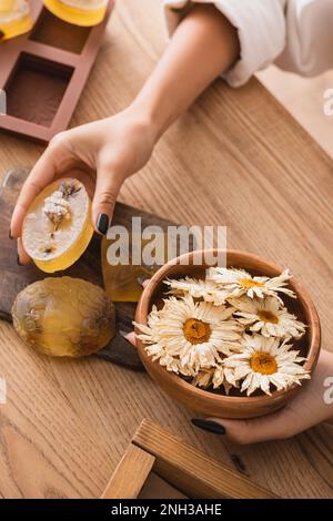 vue partielle de la femme afro-américaine tenant du savon à base de plantes et bol avec des chamomiles séchés dans l'atelier d'artisanat, image de stock Banque D'Images