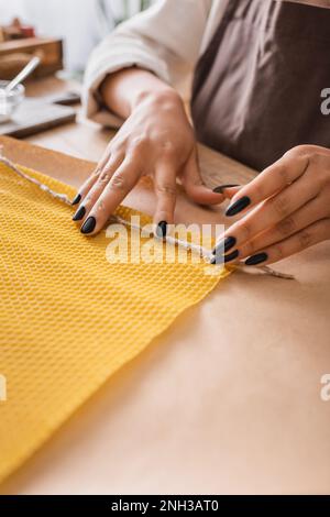 vue rognée de l'artisan afro-américain tenant la corde près de la feuille de cire tout en faisant la bougie dans l'atelier, image de stock Banque D'Images