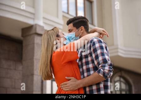 Couple dans des masques médicaux essayant de baiser à l'extérieur Banque D'Images