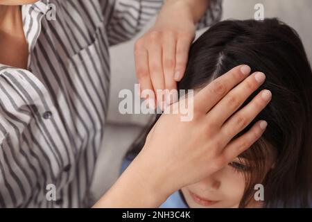 Mère examinant les cheveux de sa fille à l'intérieur. Traitement anti-poux Banque D'Images