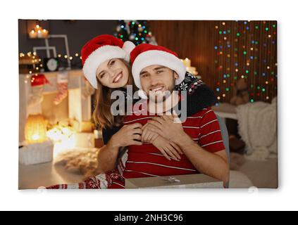 Photo imprimée sur toile, fond blanc. Joyeux jeune couple en chapeaux de père Noël célébrant Noël à la maison Banque D'Images