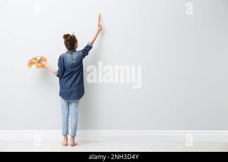 Une petite fille peint sur un mur lumineux à l'intérieur, vue arrière. Espace pour le texte Banque D'Images