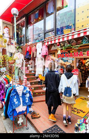 Tokyo, Harajuku, rue Takeshita. Panama Boy magasin d'occasion, extérieur. Divers vêtements et chaussures en dehors du magasin. Jeune couple tenant les mains marchant dedans. Banque D'Images