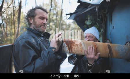 Les sans-abri réchauffent leurs mains sur la cheminée de leur cabane en hiver dans les bois. Banque D'Images