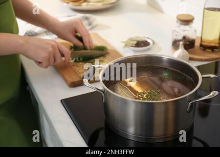 Recette de bouillon maison. Femme coupant de la verdure dans la cuisine, foyer sur pot Banque D'Images