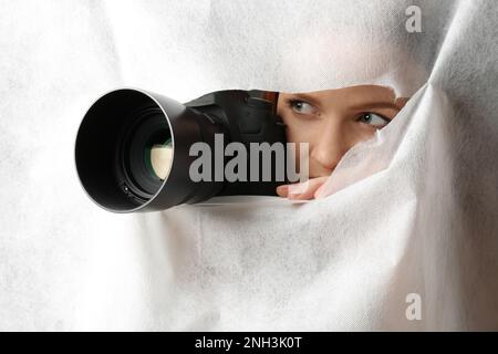 Femme cachée avec caméra espionnant par trou dans le tissu blanc Banque D'Images