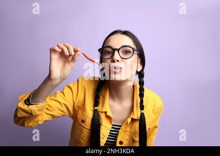 Jeune femme à la mode avec des tresses mâchant du bubblegum sur fond lilas Banque D'Images